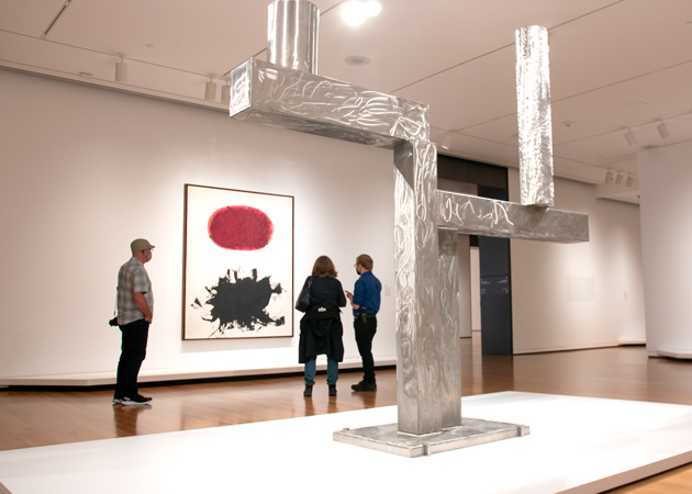 Photo of the galleries featuring a large steel sculpture and people looking at an abstract painting