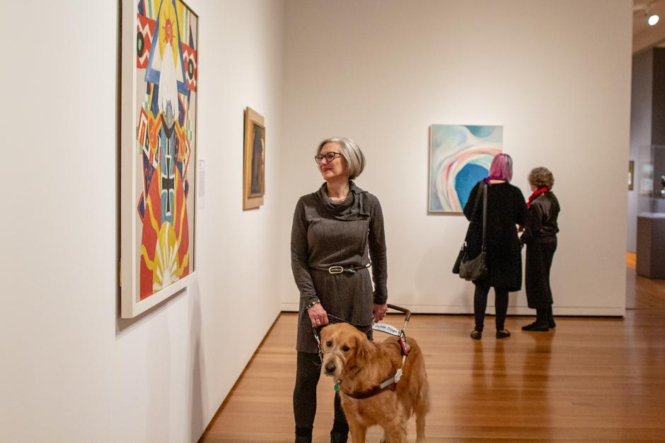 Photo of Art Beyond Sight tour participant looking at a colorful, abstract painting at the Seattle Art Museum with her guide dog.