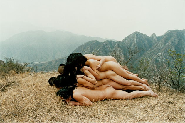 a photograph of a wide mountainous vista, with a group of people stacking their bodies in the shape of a mountain