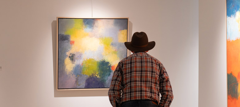 Photo of a person looking at a row of paintings in blue and yellow hung in SAM Gallery